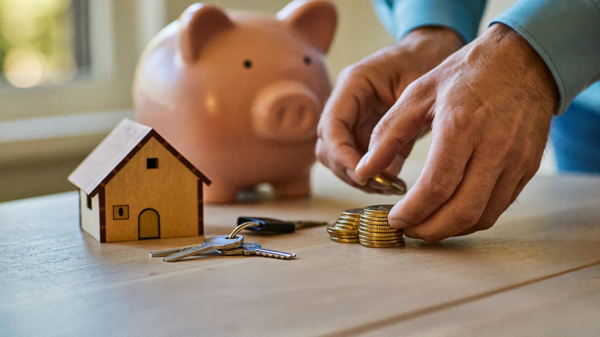 A first-time buyer counting savings at a kitchen table with a house key and calculator beside a laptop.